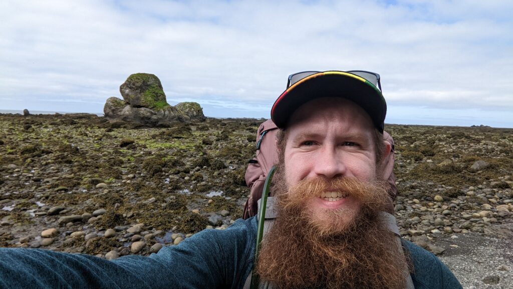 Selfie of man during his hike along coast in Oregon with rock formation behind him