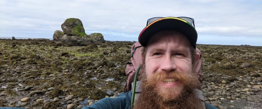 Selfie of man during his hike along coast in Oregon with rock formation behind him