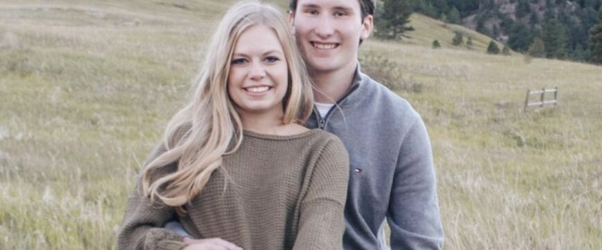 Hannah and Drew sitting on a fence with a green field and trees in the background