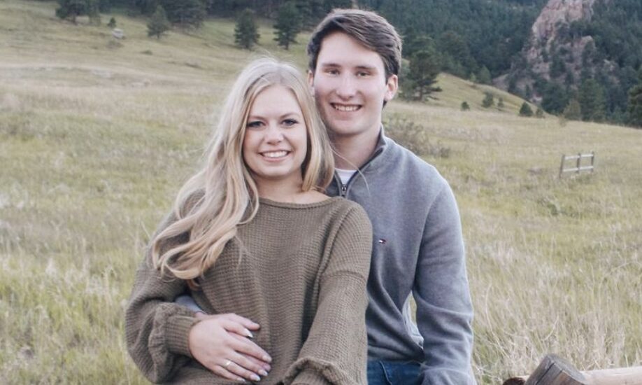 Hannah and Drew sitting on a fence with a green field and trees in the background